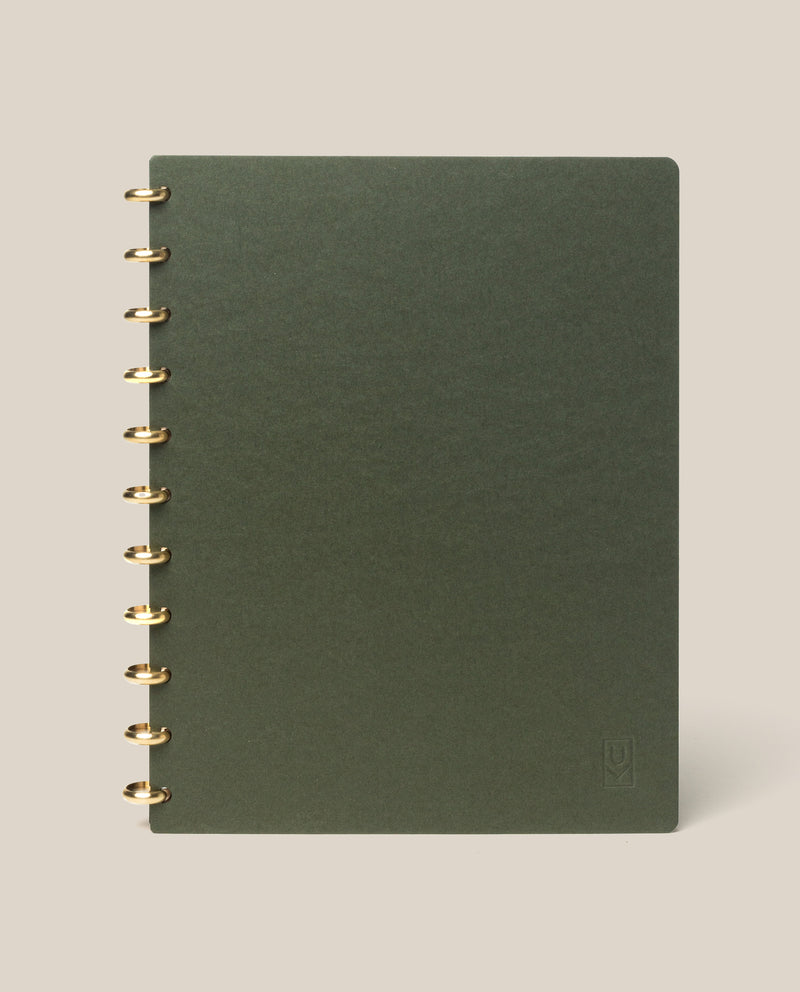 A large (8.5" x 11") Discbound Journal with a green plain cover and gold rings, refillable and spiral-bound, shown on a light beige background.