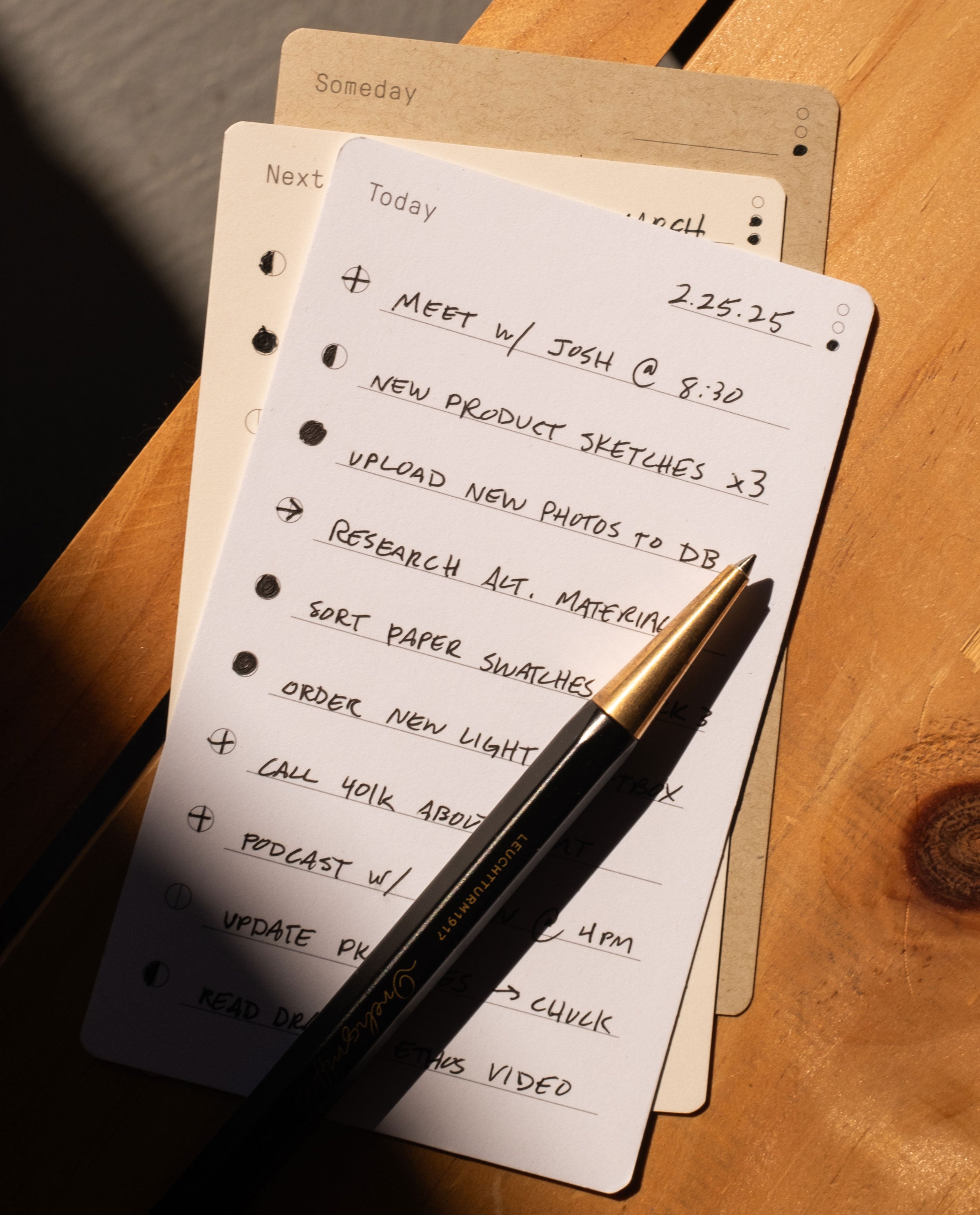 The Analog Trial Pack features a handwritten to-do list on premium card stock with a black and gold pen, resting on a wooden table. Also included are 3x5 notecard planners labeled Someday and Next, partially visible underneath.