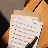 The Analog Daily Focus Kit (Walnut) displays a handwritten to-do list with tasks like meeting with Josh, product sketches, and uploading photos on a wooden surface beside a black pen and additional task cards for organized productivity.