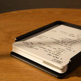 The Analog Capture Kit - 2 Large (Black Aluminum) sits on a wooden table, holding a stack of dot grid cards filled with handwritten black ink notes and drawings. A black pen rests nearby.