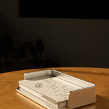A silver aluminum Analog Capture Kit - Small sits on a wooden table, holding dot grid cards. Sunlight creates warm shadows while a few extra cards from the kit are scattered close by. The background is dark and blurred.