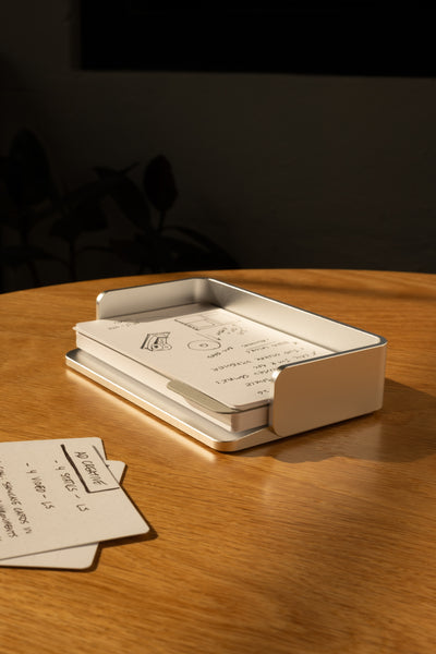 A silver aluminum Analog Capture Kit - Small sits on a wooden table, holding dot grid cards. Sunlight creates warm shadows while a few extra cards from the kit are scattered close by. The background is dark and blurred.
