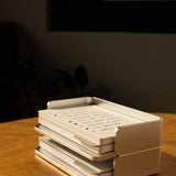 A stack of handwritten cards from the Analog Capture Kit - Small (Silver Aluminum) sits in its sleek tray on a wooden table, bathed in sunlight—perfect for capturing inspired thoughts.