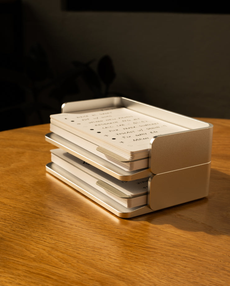 A stack of handwritten cards from the Analog Capture Kit - Small (Silver Aluminum) sits in its sleek tray on a wooden table, bathed in sunlight—perfect for capturing inspired thoughts.