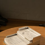 The Analog Capture Kit - Small (Silver Aluminum) with dot grid cards sits on a wooden table. A black and gold pen lies in front, while warm sunlight highlights the inviting setup, perfect for capturing hand-drawn diagrams and notes.