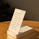 The Analog Daily Focus Kit + 6 Refills (Silver Aluminum) holds a handwritten to-do list in its minimalist card holder on a wooden table, bathed in warm sunlight, with additional task cards neatly stacked inside.