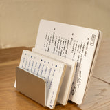 The Complete Analog Collection (Silver Aluminum) minimalist metal desktop organizer neatly holds multiple open notebooks of various sizes, filled with handwritten notes and sketches, on a wooden surface.