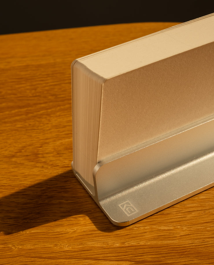 A thick paperback book stands upright in the Analog Weekly Planning Kit (Silver Aluminum) on a wooden surface, casting a soft shadow—ideal for keeping your week’s plans and cards organized and easily visible.