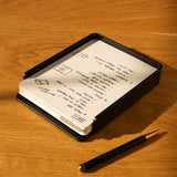 The Analog Capture Kit - Large (Black Aluminum) features a black aluminum card tray holding dot grid cards with handwritten notes and sketches. A black pen with a gold tip sits on a light wooden surface next to the kit.