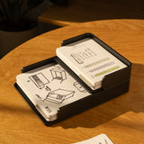 The Analog Capture Kit - Small & Large (Black Aluminum) rests on a wooden table beside an open notebook with colorful sketches and a green marker, as sunlight casts warm shadows over this creative setup.