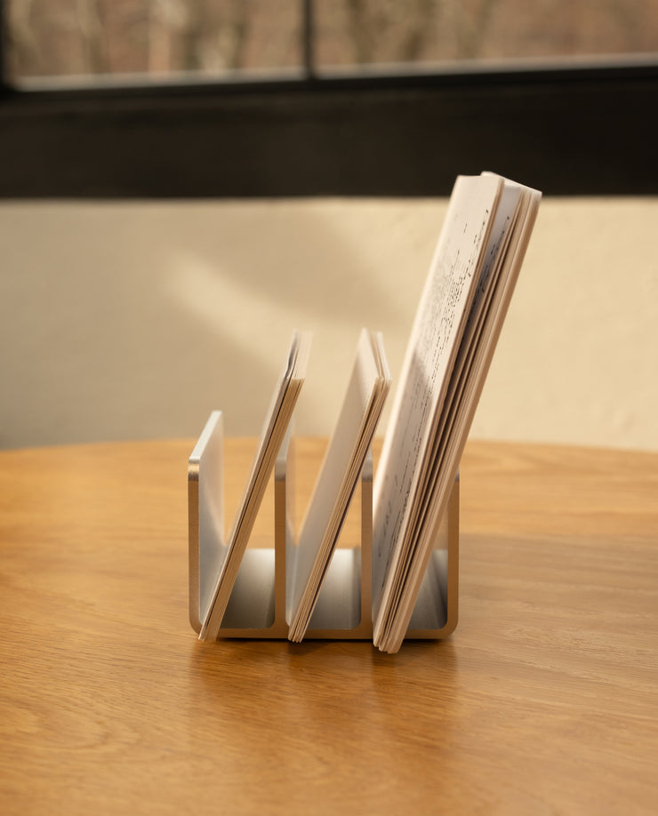 An Analog Card Organizer (Silver Aluminum) sits on a wooden table, neatly storing cards and papers, with a window and blurred outdoor scenery visible in the background.