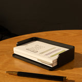 The Analog Capture Kit - Small (Black Aluminum) with a stack of Dot Grid Cards and a black pen sits on a round wooden table in warm light.