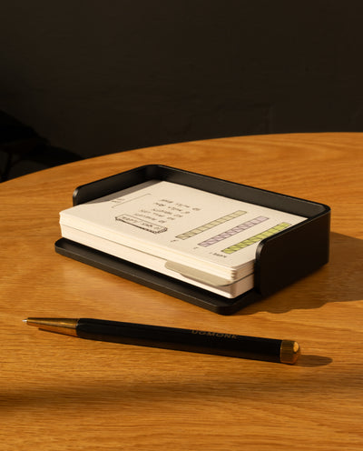 The Analog Capture Kit - Small (Black Aluminum) with a stack of Dot Grid Cards and a black pen sits on a round wooden table in warm light.