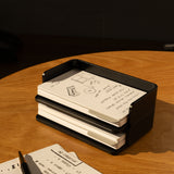An Analog Capture Kit - Small (Black Aluminum) sits on a wooden table, holding Dot Grid Cards. The top card features sketches and notes; nearby, a pen and two more notecards from the kit with handwritten notes are partly visible.