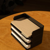 A black Analog Capture Kit - Small (Black Aluminum) holds stacks of brown and white Dot Grid Cards on a wooden table in warm sunlight.