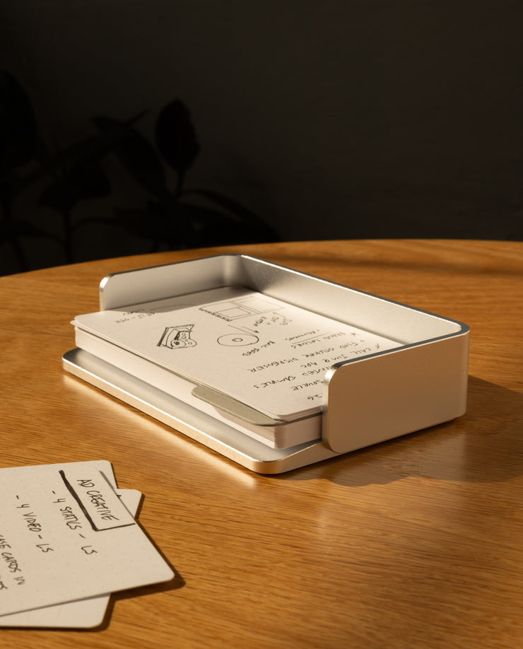 The Complete Analog Collection (Silver Aluminum) rests on a wooden table, holding handwritten notes and sketches in warm sunlight, with extra index cards neatly arranged beside this elegant aluminum organizer.