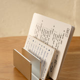 The Analog Card Organizer (Silver Aluminum) holds an open notebook with handwritten notes and sketches, displayed on a wooden surface against a beige background.