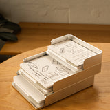 The Analog Capture Kit - 2 Large (Silver Aluminum) sits on a wooden desk, holding illustrated instruction cards. A black and gold pen is nearby, with part of a gray item and a light-colored wall in the background.