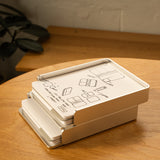 A silver aluminum Analog Capture Kit - 2 Large sits slightly open on a wooden table, with illustrated instructions on the lid. Dot grid cards and an aluminum tray are visible inside, and a leafy plant appears in the background.