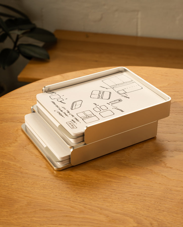 A silver aluminum Analog Capture Kit - 2 Large sits slightly open on a wooden table, with illustrated instructions on the lid. Dot grid cards and an aluminum tray are visible inside, and a leafy plant appears in the background.