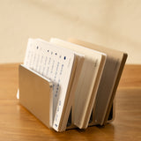 The Analog Card Organizer (Silver Aluminum) holds index cards with handwritten notes, fanned out and labeled by day, resting on a wooden surface.