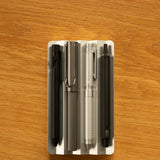 Four pens in black, gray, silver, and dark gray are neatly arranged side by side in the Analog Multi Pen Tray (Silver Aluminum) on a wooden surface.
