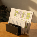 The Complete Analog Collection (Black Aluminum) holds two open notebooks on a wooden desk, one featuring colorful diagrams and the other with handwritten notes. Sunlight from a window casts warm shadows across the organized workspace.