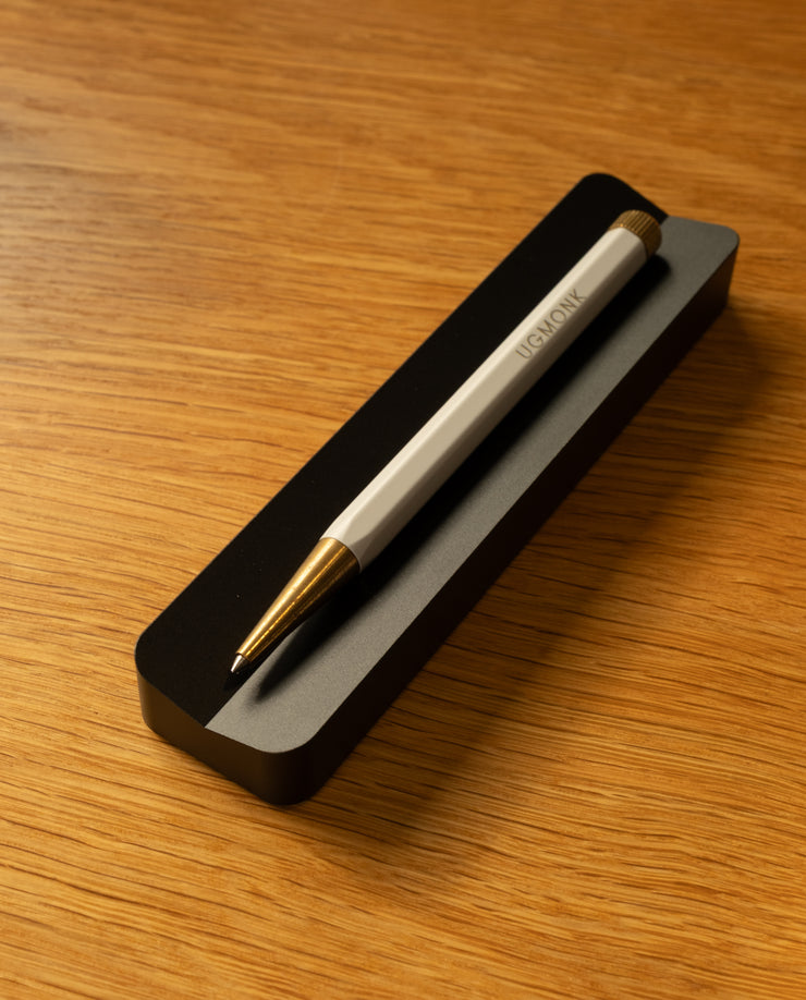 A pen from The Complete Analog Collection (Black Aluminum) rests diagonally on a black rectangular holder atop a warm wooden surface—perfect for enhancing any desktop organizer setup.