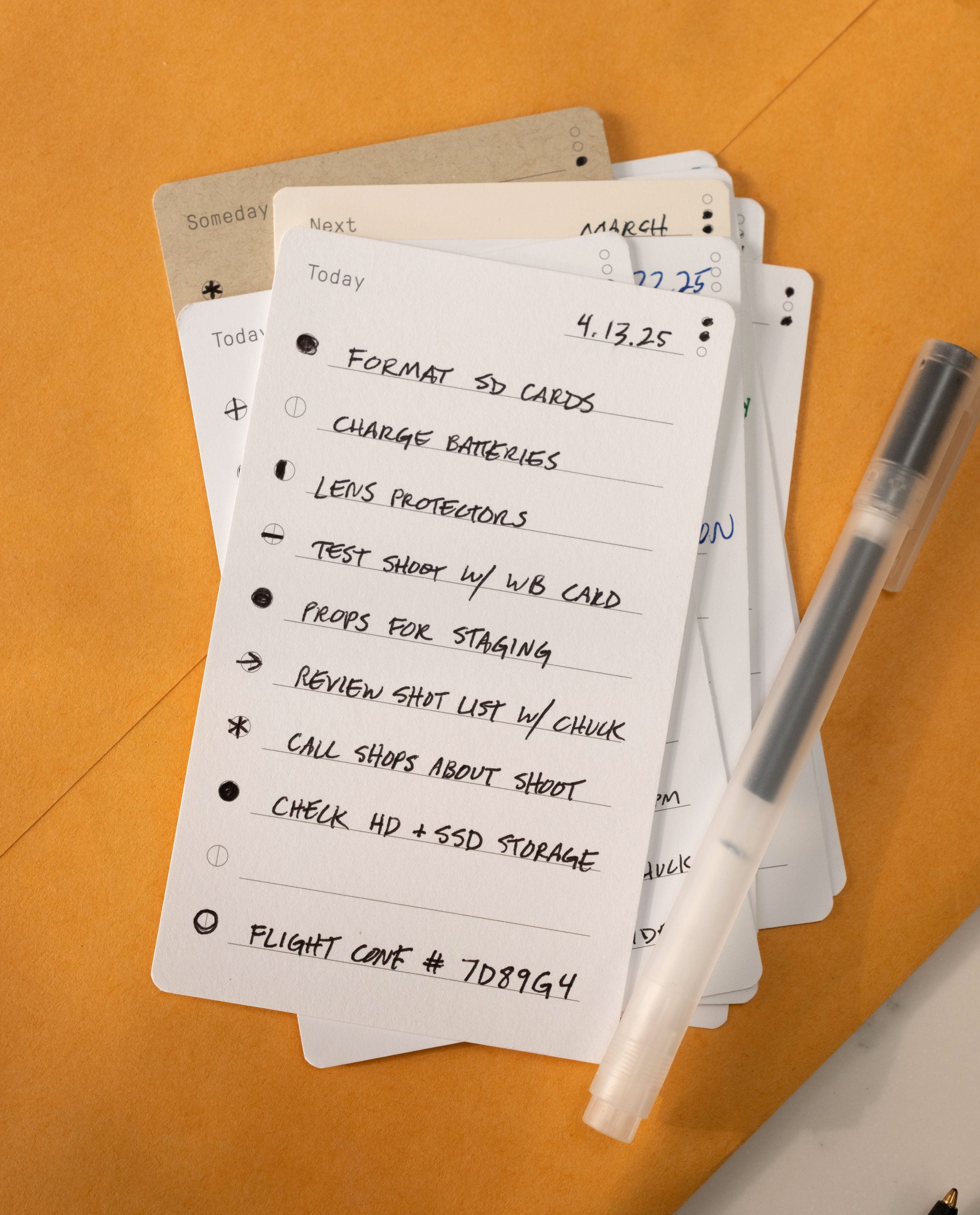 A close-up of a handwritten to-do list on premium Analog Trial Pack card stock, featuring photo shoot tasks and a pen, with other 3x5 cards partially visible underneath on an orange surface. The date 4.13.25 is at the top.