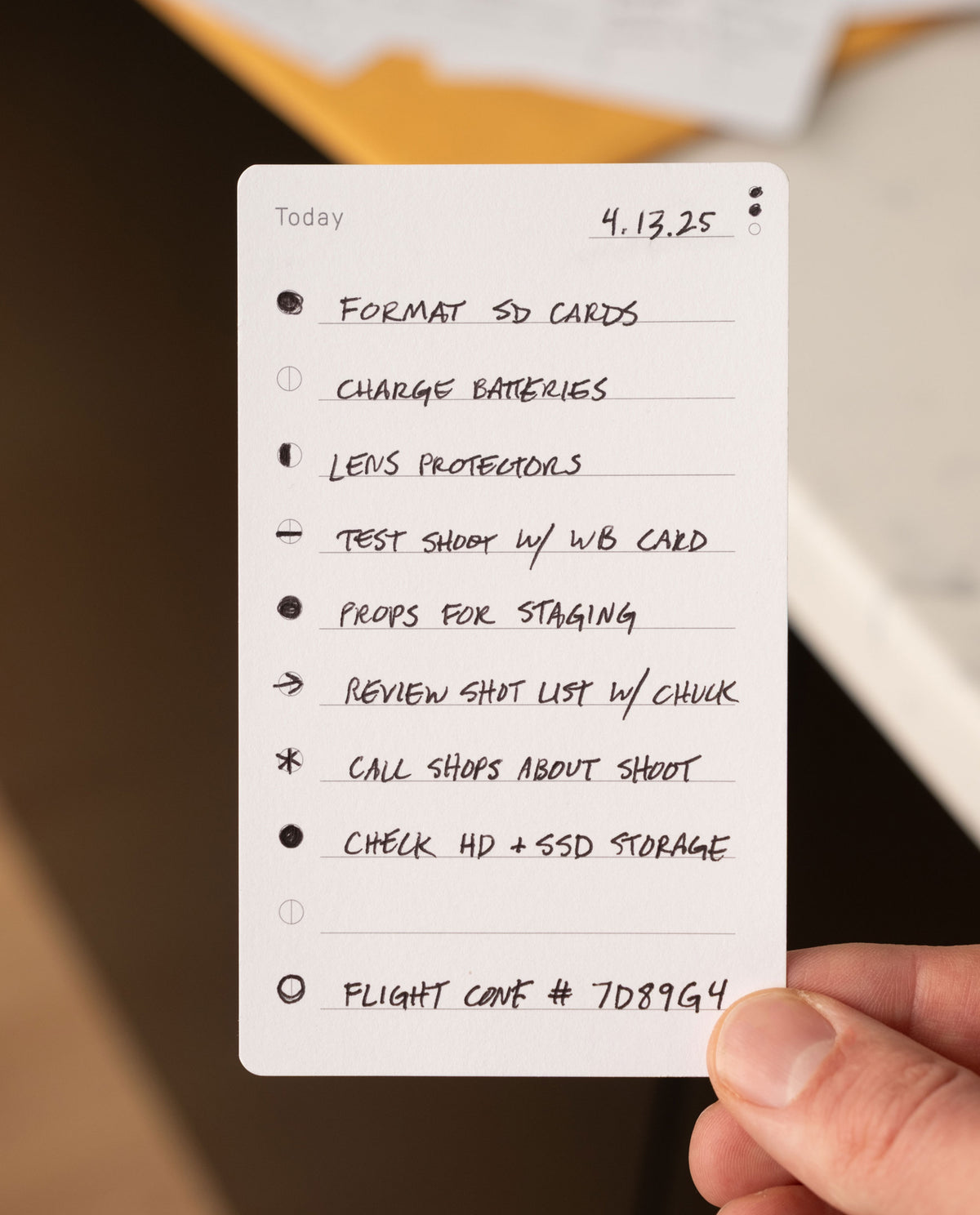 A hand holds an Analog - Today Card dated 4.13.25, displaying a well-organized productivity system with tasks such as formatting SD cards, charging batteries, prepping props, reviewing a shot list, and FLIGHT CASE #708964 noted at the bottom.