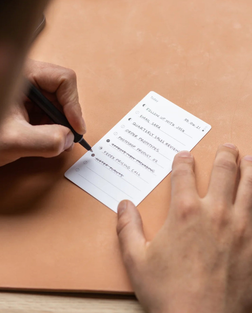 Using a black pen, someone writes tasks like “Follow up with Jim” and “Schedule meeting” on a small, white 3x5 card from the Analog Trial Pack, placing the premium card stock on a light brown surface.