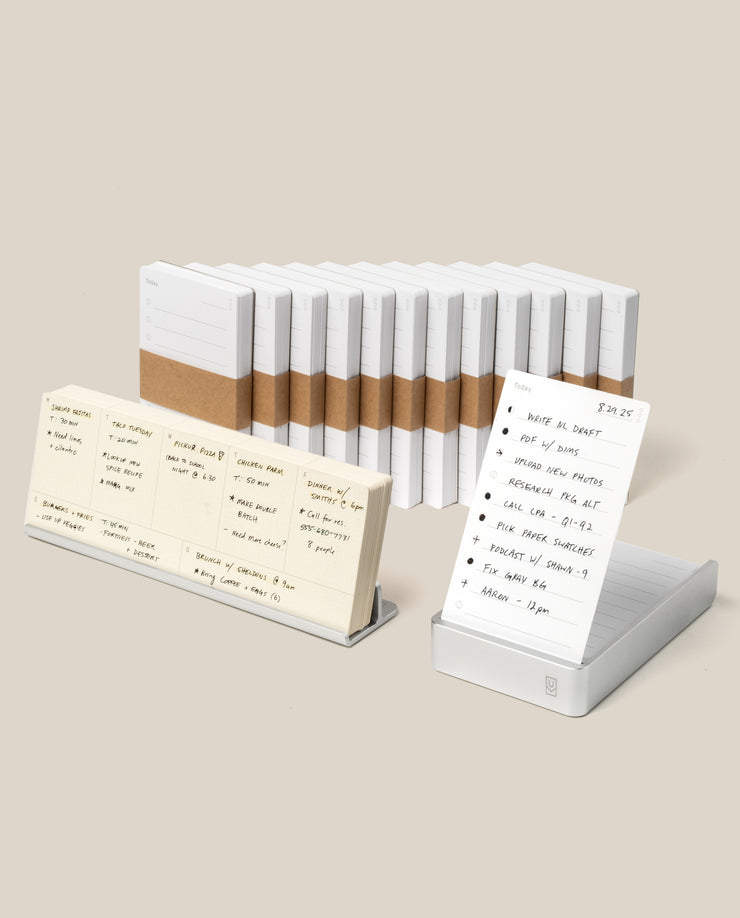 The Analog Annual Kit (Silver Aluminum) features stacked white notepads with brown bands and a card-style notepad in a clear, angled Weekly Card Holder, all presented on a neutral background.