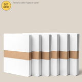 Six Analog Dot Grid Cards - Large (6-Pack) with white covers and a brown paper band are arranged in a row on a beige background. Previously called Capture Cards, they’re made from premium card stock and measure 5 x 6.5 inches.