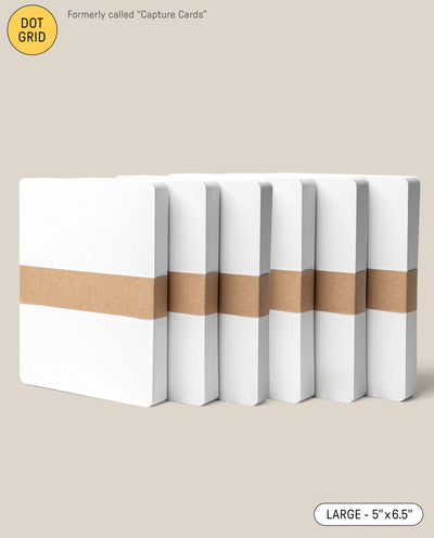 Six Analog Dot Grid Cards - Large (6-Pack) with white covers and a brown paper band are arranged in a row on a beige background. Previously called Capture Cards, they’re made from premium card stock and measure 5 x 6.5 inches.