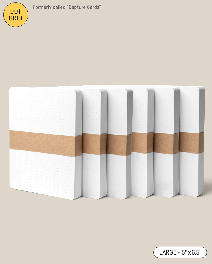 Six Analog Dot Grid Cards - Large (6-Pack) with white covers and a brown paper band are arranged in a row on a beige background. Previously called Capture Cards, they’re made from premium card stock and measure 5 x 6.5 inches.