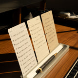 A desk organizer holding three handwritten to-do lists and a pen sits on a wooden desk beside a computer keyboard, bathed in warm sunlight.