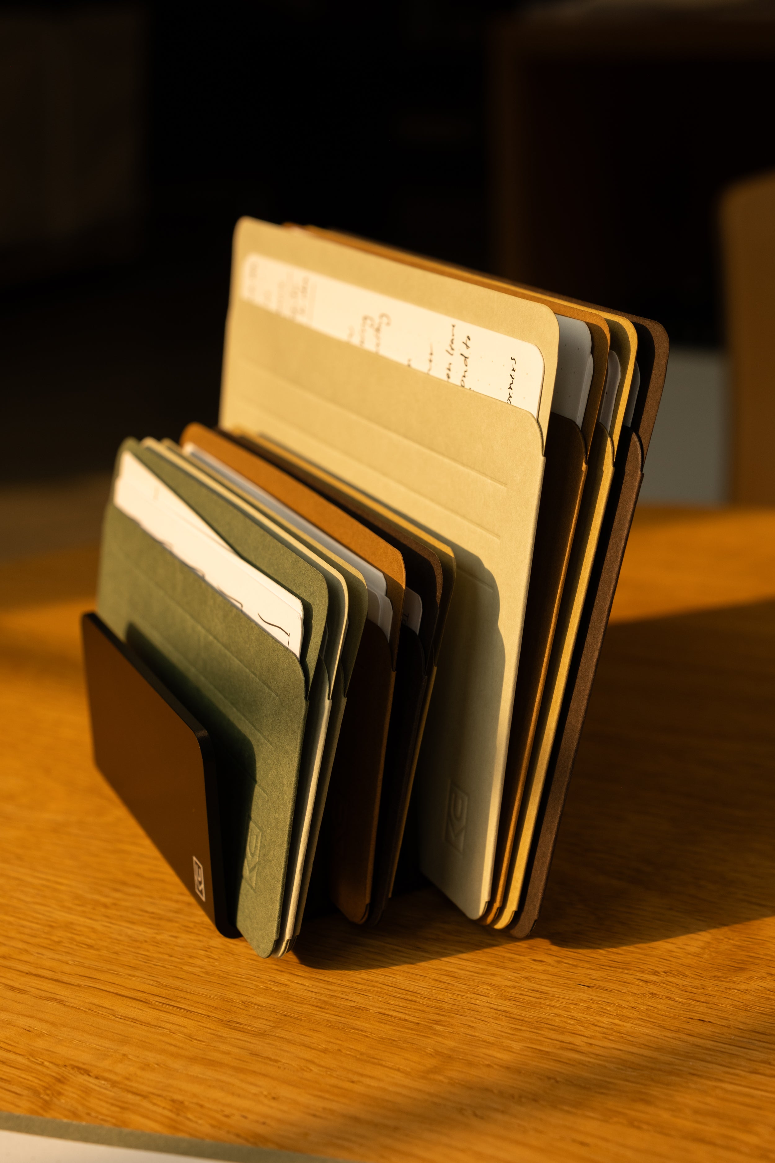 A set of assorted folders and documents, together with Analog Card Sleeves - Large (Earth), is organized in a vertical file holder that sits on a wooden desk, warmly illuminated by sunlight.