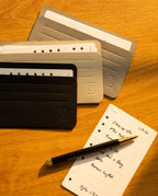 A black pen rests on a notepad with a handwritten to-do list, next to four Analog Card Sleeves - Small (Monochrome) card organizers on a wooden surface.