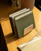 A set of file folders organized in a holder sits on a wooden desk, with sunlight streaming in. Analog Card Sleeves - Large (Earth) add a touch of order among the folders, while another folder lies flat in the foreground.