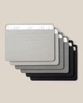 Six Large Analog Card Sleeves (Set of 6 – Monochromatic) in minimalist rectangular shapes and shades of grey and black are stacked in a fan arrangement, each organizer displaying handwritten notes peeking from the top.