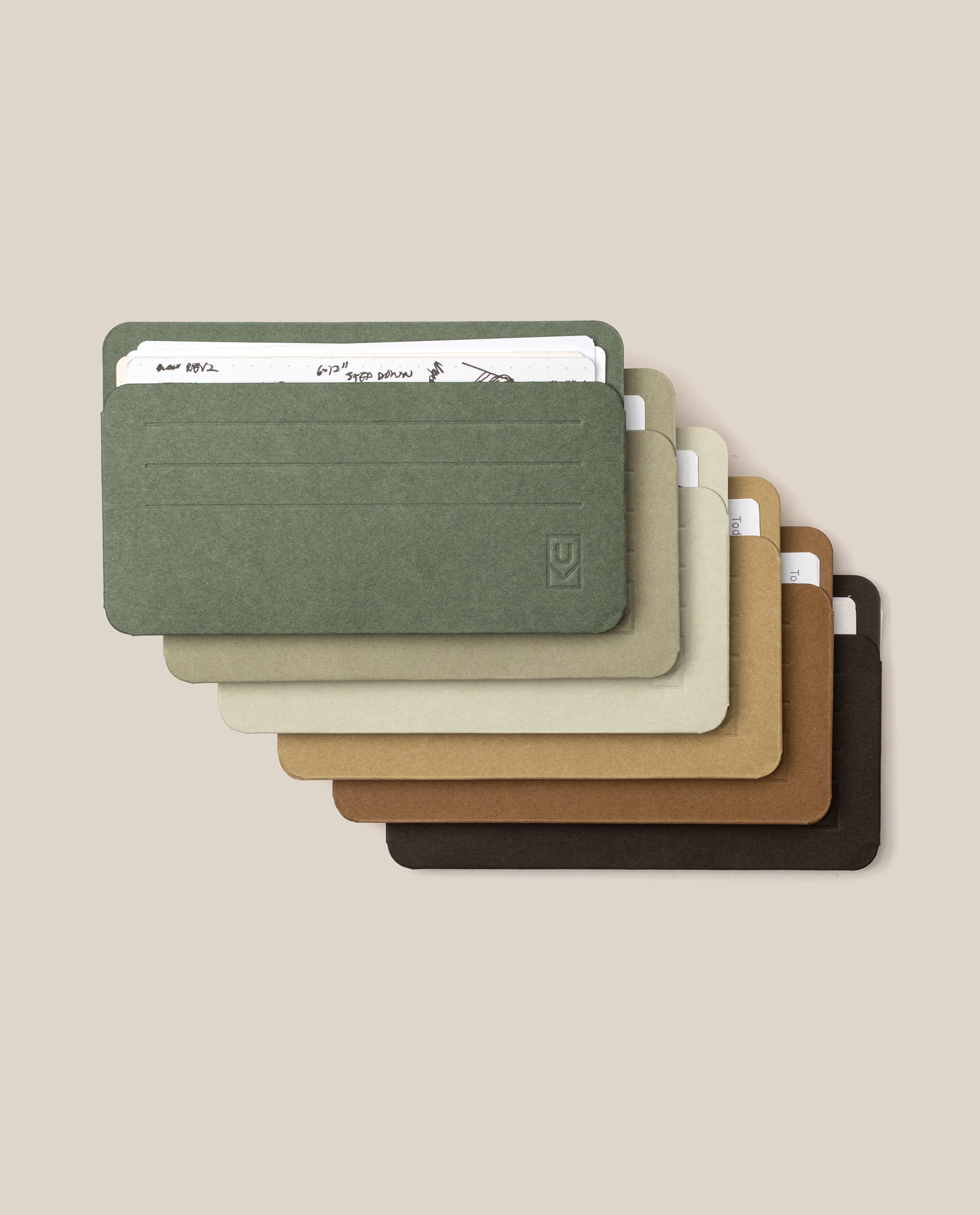 Six Small Analog Card Sleeves (Set of 6 - Earth tones) in shades of green, beige, tan, and brown are stacked in a fanned arrangement on a neutral background, each serving as a sleek card organizer while holding papers or cards.