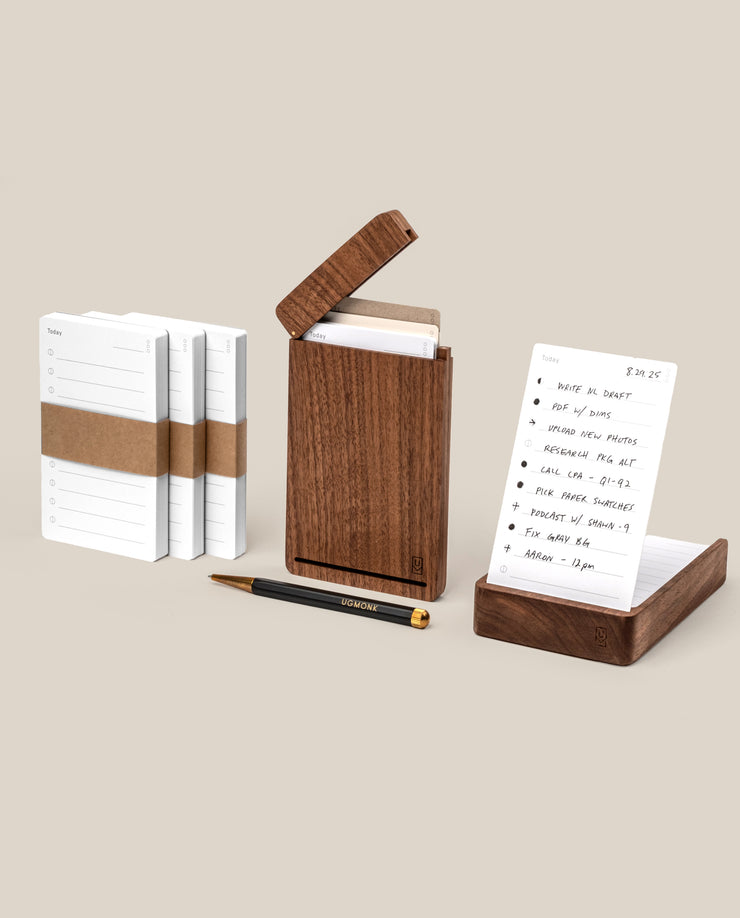 The Analog Complete Kit (Walnut) features a walnut desktop card holder with white notecards—some stacked, some displayed—a sleek black and gold refillable gel pen, and a light beige background. A notecard displays handwritten notes.