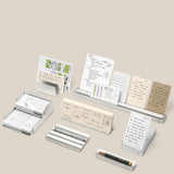 A neatly arranged set from The Complete Analog Collection (Silver Aluminum) displays notecards, papers, and pens on a neutral background, with handwritten notes and schedules in white and beige tones held tidily in minimalist organizers.