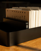 An Analog Archive (Black Aluminum) desk organizer holding a row of white index cards with printed labels.