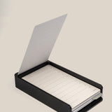 The Analog Daily Focus Kit + 6 Refills (Black Aluminum) features a sleek black rectangular box holding a notepad with lined, numbered sheets; one sheet is flipped open and stands upright.