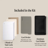 The Analog Daily Focus Kit + 3 Refills (Black Aluminum) display shows a 1 Month of Task Cards stack, a gray card divider, and a black aluminum holder with front slot and back storage. Labels explain the use of each item.