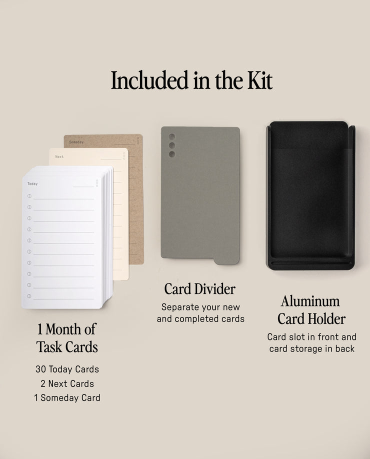 The Analog Daily Focus Kit + 3 Refills (Black Aluminum) display shows a 1 Month of Task Cards stack, a gray card divider, and a black aluminum holder with front slot and back storage. Labels explain the use of each item.