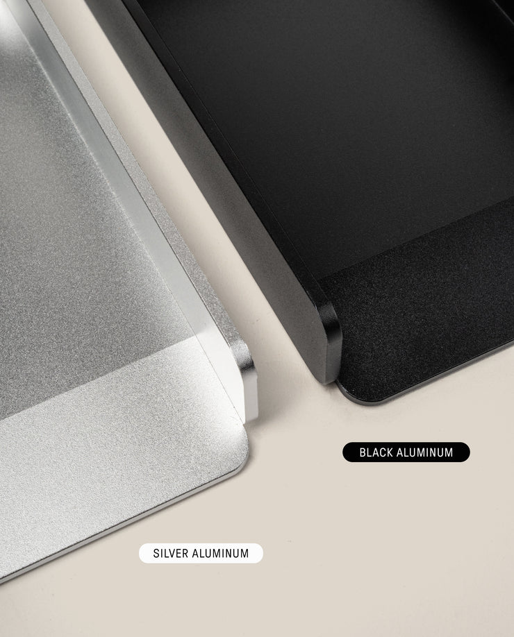 Close-up of two rectangular metal trays, one in silver and one in black aluminum, side by side on a light surface; the silver tray is the Analog Daily Focus Kit (Silver Aluminum) with labeled colors.