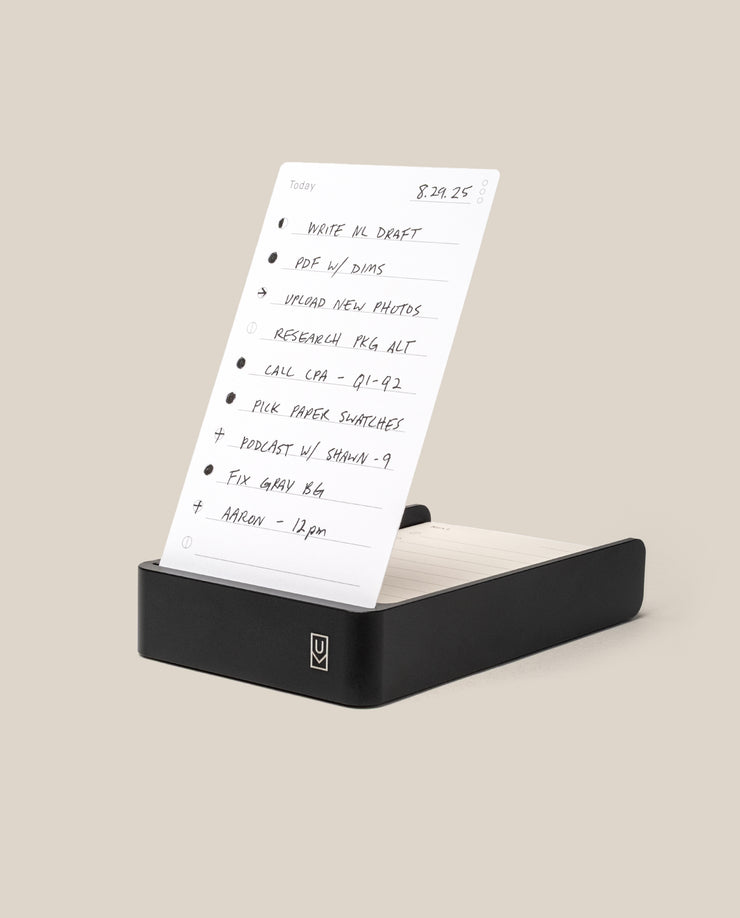 The Analog Daily Focus Kit (Black Aluminum) holds a handwritten to-do list on a white task card with tasks, times, and checkboxes, set against a beige background—ideal for organizing your productivity system.