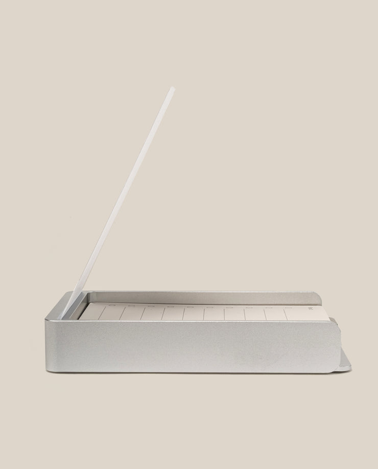 The Analog Daily Focus Kit + 6 Refills (Silver Aluminum) is a minimalist desk organizer that holds a notepad and white pencil upright, keeping task cards tidy on your workspace, shown against a plain beige background.